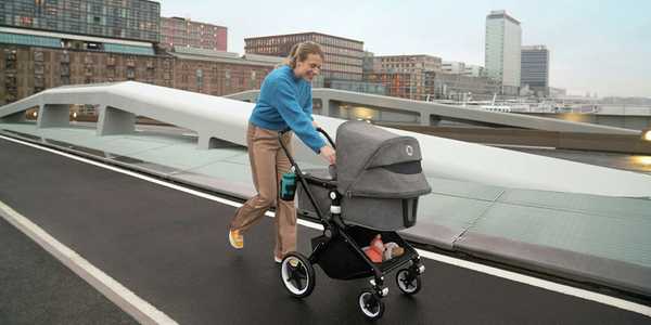 A woman walking her baby in a Bugaboo Lynx pushchair in black and grey colour.